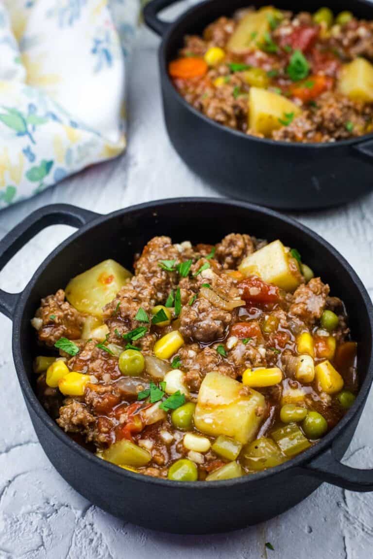 Two bowls of Easy Hamburger Stew, featuring potatoes, peas, corn, carrots, and garnished with parsley.