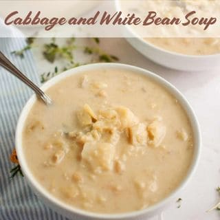 A bowl of cabbage and white bean soup with a spoon, garnished with herbs.
