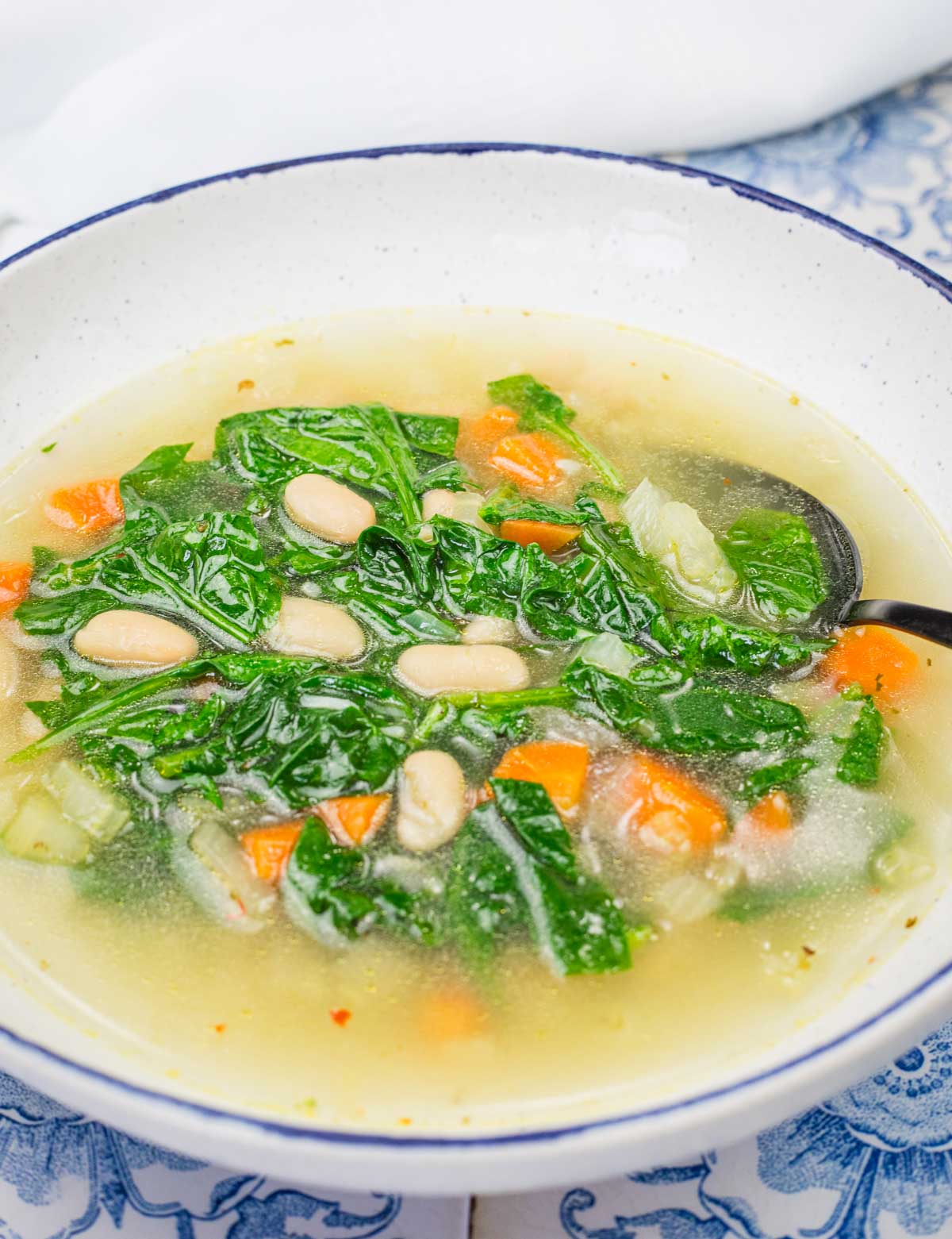 A bowl of Rice and White Bean Soup containing white beans, kale, carrots, and other vegetables, with a spoon on the side.