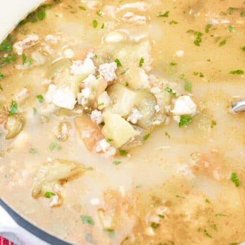 A pot of Green pork posole soup with ground meat, vegetables, herbs, and broth, with a metal ladle resting inside.